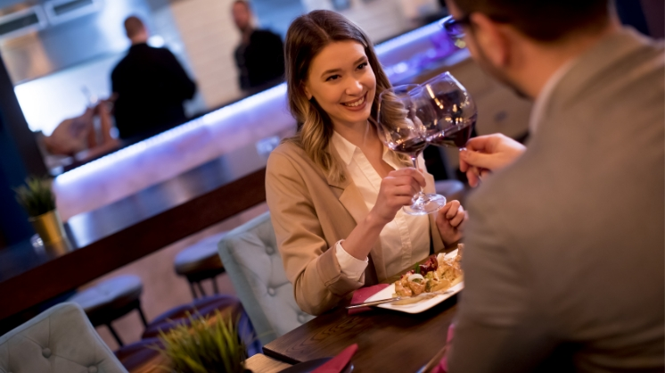 Mujer sonriendo brindando con copa de vino en restaurante con hombre