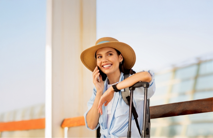 Mujer sonriente con sombrero y maleta hablando por teléfono
